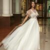 Cape sleeved wedding dress with illusion neckline and floral appliqué across the bodice