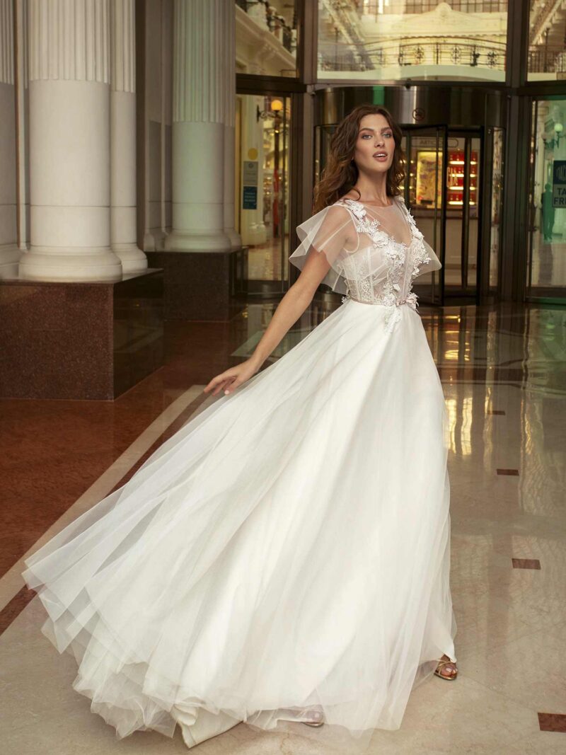 Cape sleeved wedding dress with illusion neckline and floral appliqué across the bodice