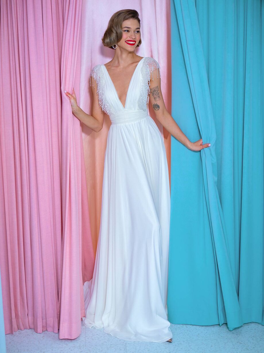 Front view of a sheath wedding gown with beaded fringe sleeves, featuring a deep V neckline and flowing chiffon skirt, available at Papilio Boutique bridal store in Toronto.