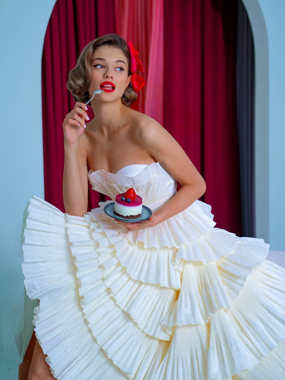 Playful tea-length wedding dress with tiered pleated taffeta, strapless bodice, and belt detail, available at Papilio Boutique.