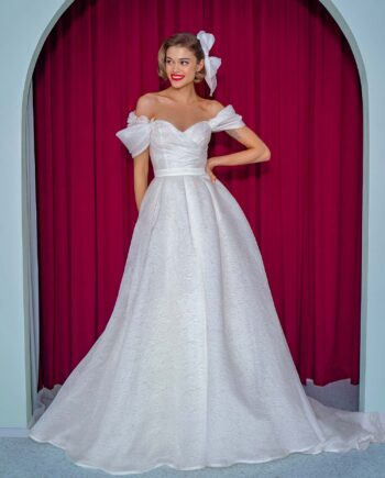 A model showcasing a white ball gown with off-the-shoulder straps, a sweetheart neckline, and a voluminous textured organza skirt. This elegant bridal gown is available at Papilio Boutique in Toronto.