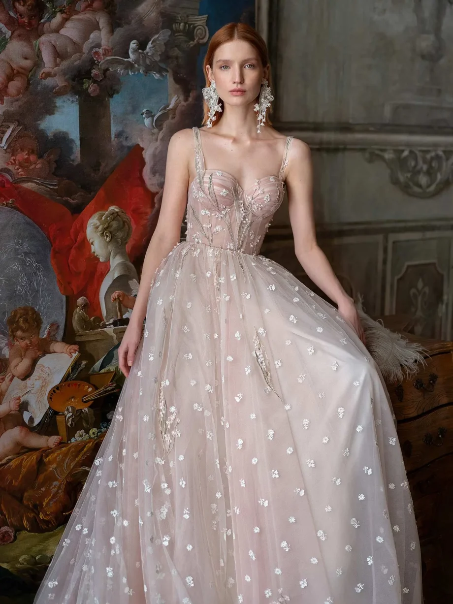 Front view of a bride in a pink-ivory ballgown with a floral design and semi-sheer corset, part of the Papilio Boutique sample sale in Toronto, standing against an artistic, baroque backdrop, embodying classical elegance.