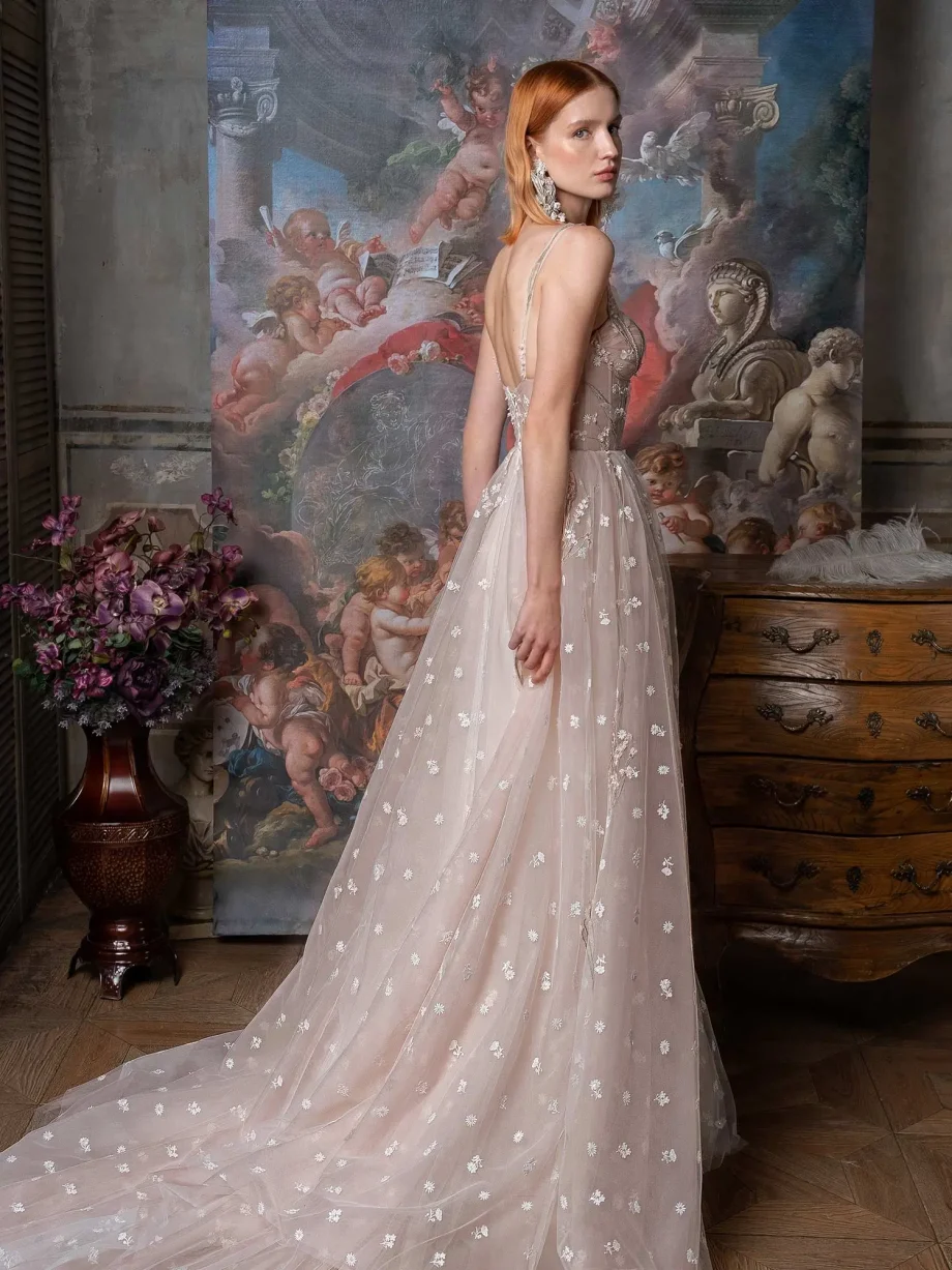 Side view of a bride in a pink-ivory ballgown showcasing the delicate lace-up back of the semi-sheer corset and the expansive floral tulle train, available in the Papilio Boutique sample sale in Toronto, set in a richly decorated vintage setting.