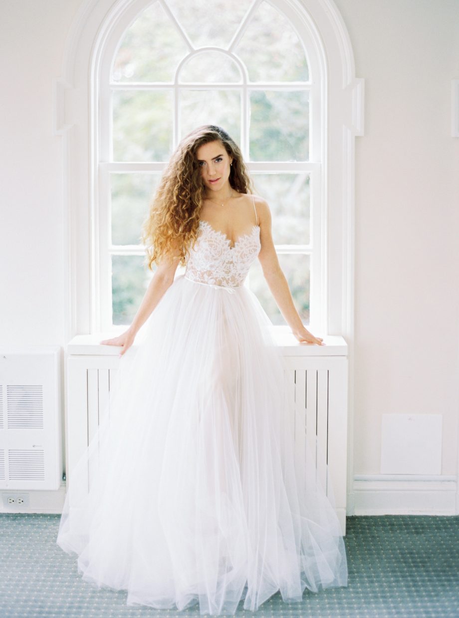 Front view of a simple ballgown wedding dress with lace bustier corset, spaghetti straps, and full ivory tulle skirt over nude lining, available at Papilio Boutique's sample sale in Toronto