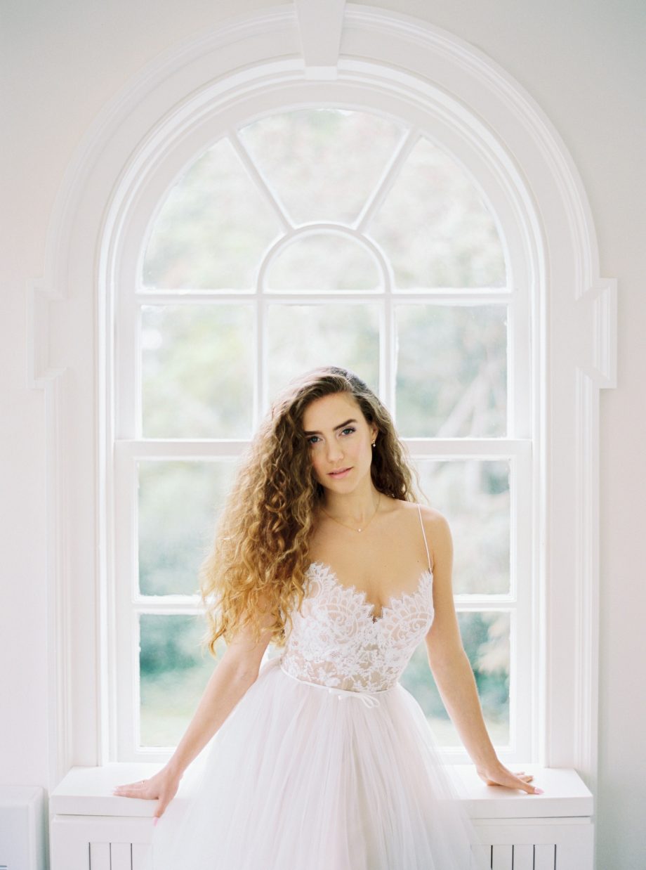 Front view of a simple ballgown wedding dress with lace bustier corset, spaghetti straps, and full ivory tulle skirt over nude lining, available at Papilio Boutique's sample sale in Toronto