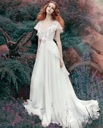 A bride wearing a bohemian sheath wedding dress with ruffled short sleeves and lace detailing, standing in a dreamy outdoor setting. Perfect for bohemian wedding dresses Toronto.