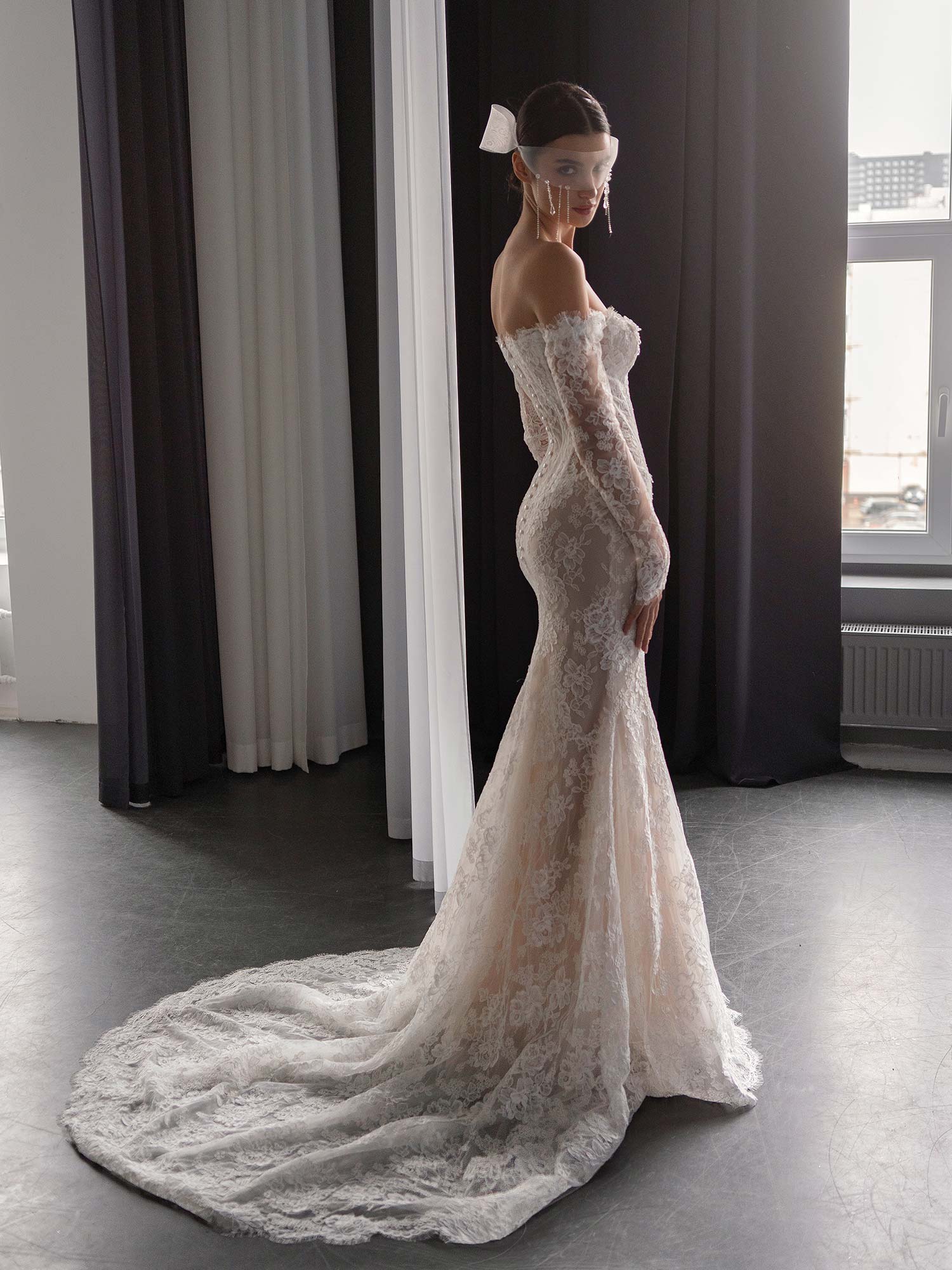 Side profile of lace drop waist fit and flare wedding dress with long sleeves and dramatic train, BY Papilio Boutique, Toronto bridal shop.